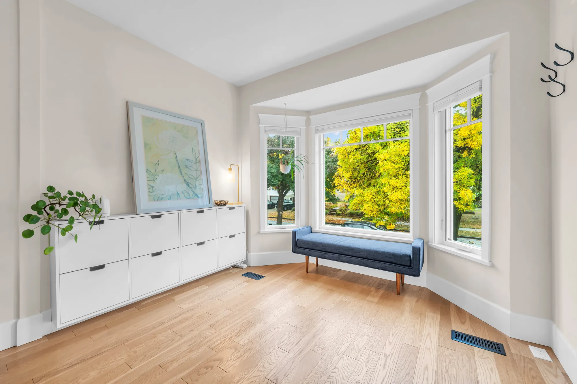The bay window with a cushioned bench, a long white low cabinet with a painting above it, a stained-glass window