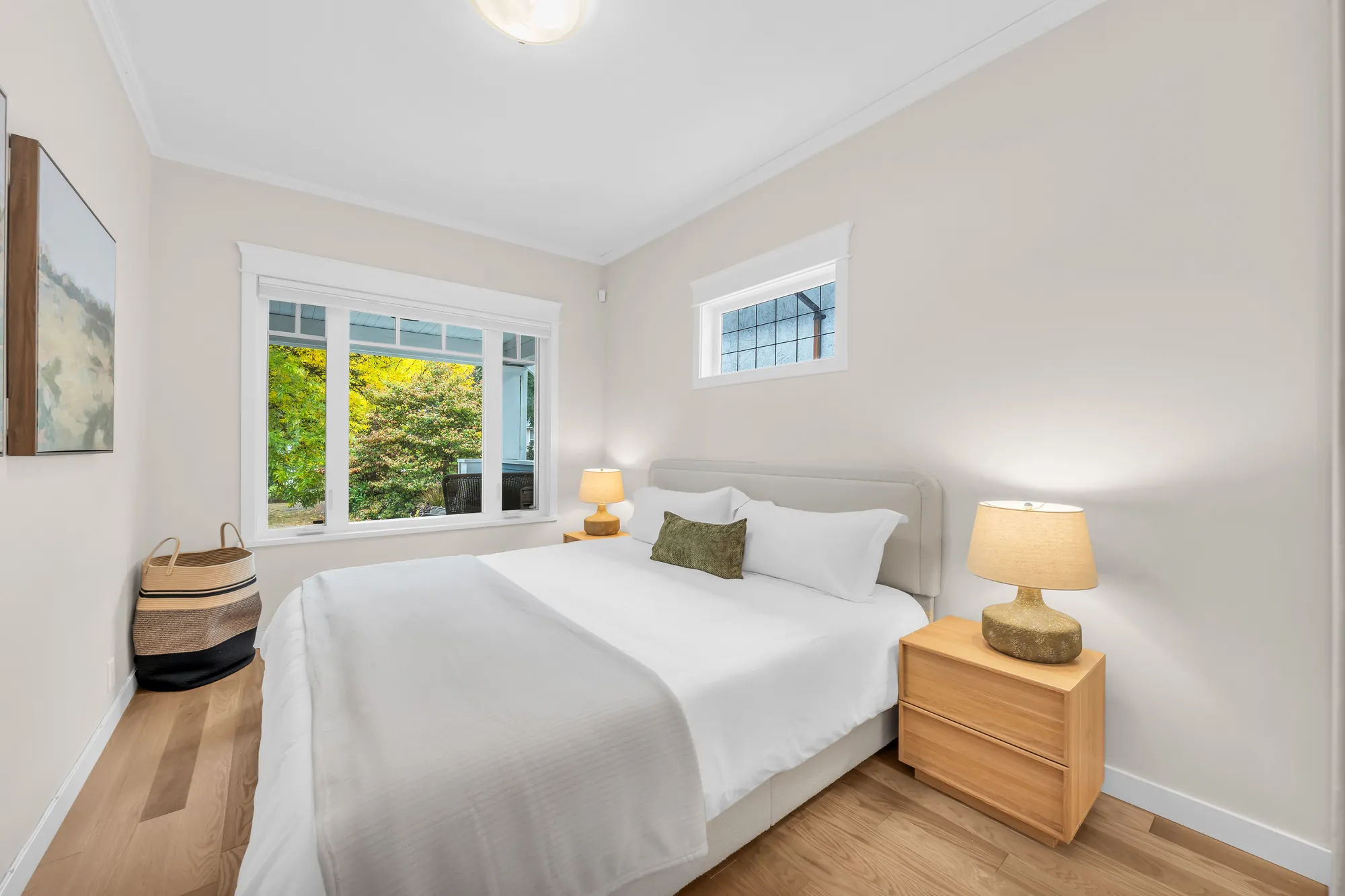 The back bedroom: a queen bed with white linen, wood night tables with lamps, a window and a small high window