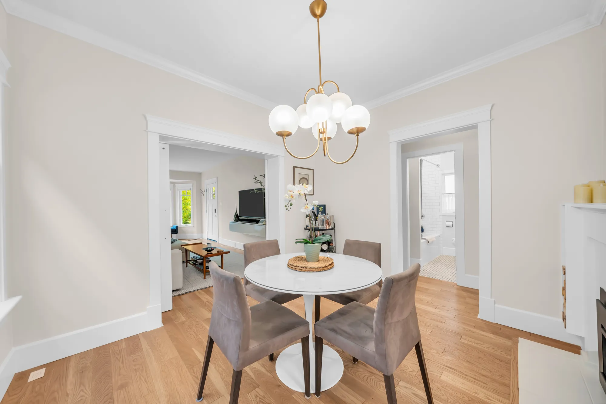 The dining room toward the living room through the wide opening, the round table and chairs, the chandelier
