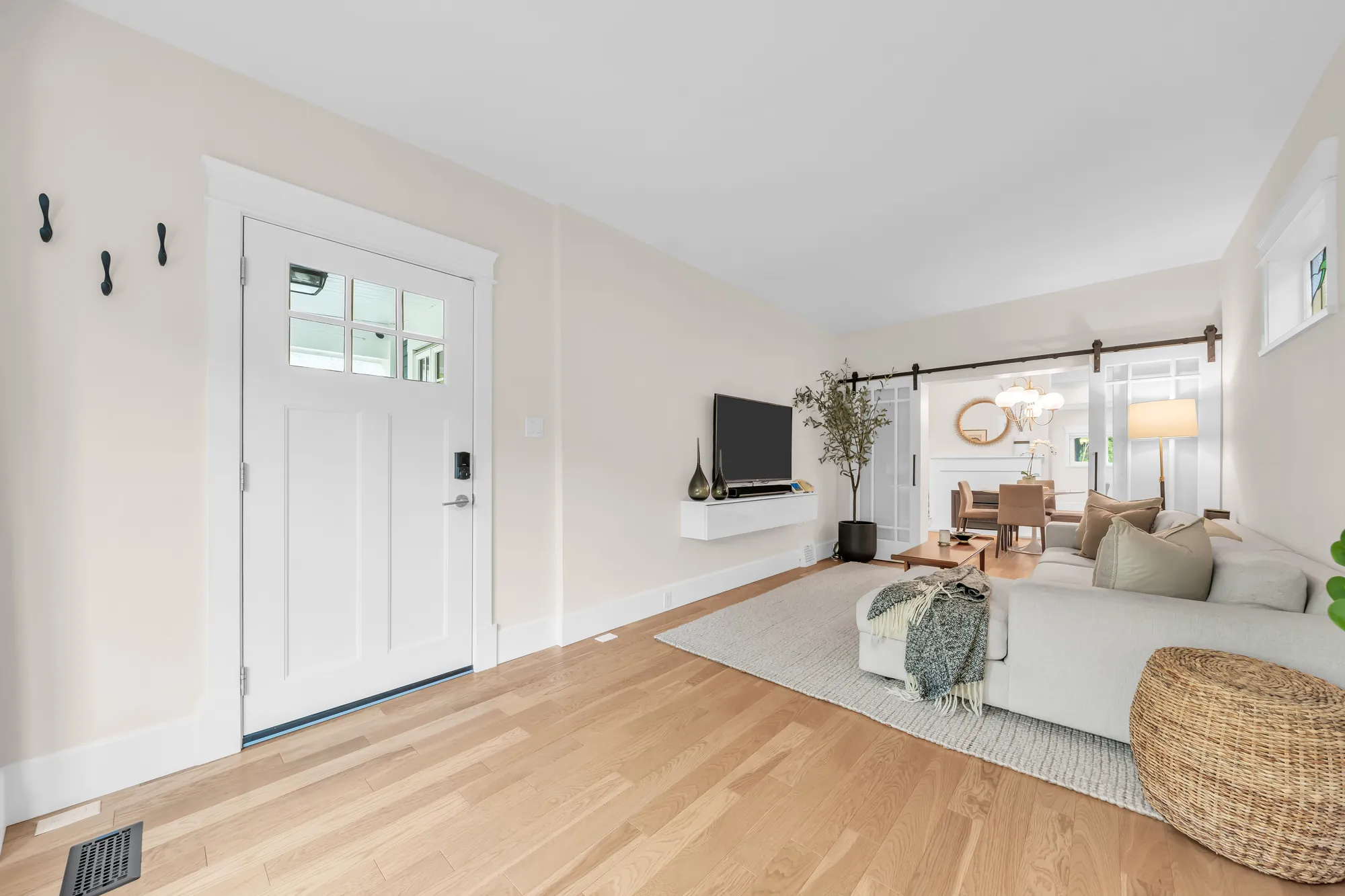 The front door, white with a glass panel, opening into the living room, the dining room beyond the barn doors