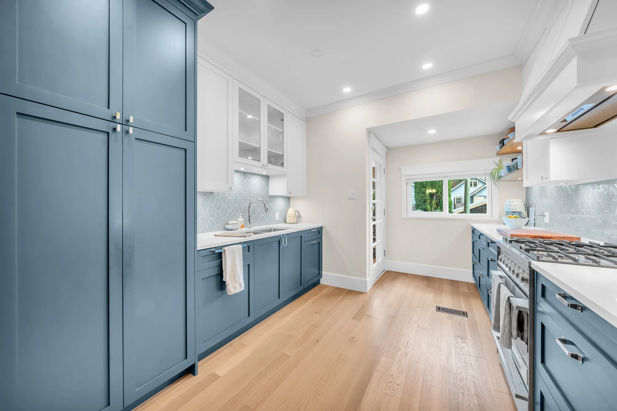 Along the kitchen to the window: tall blue pantry cabinets at the left, the sink counter, the range at the right