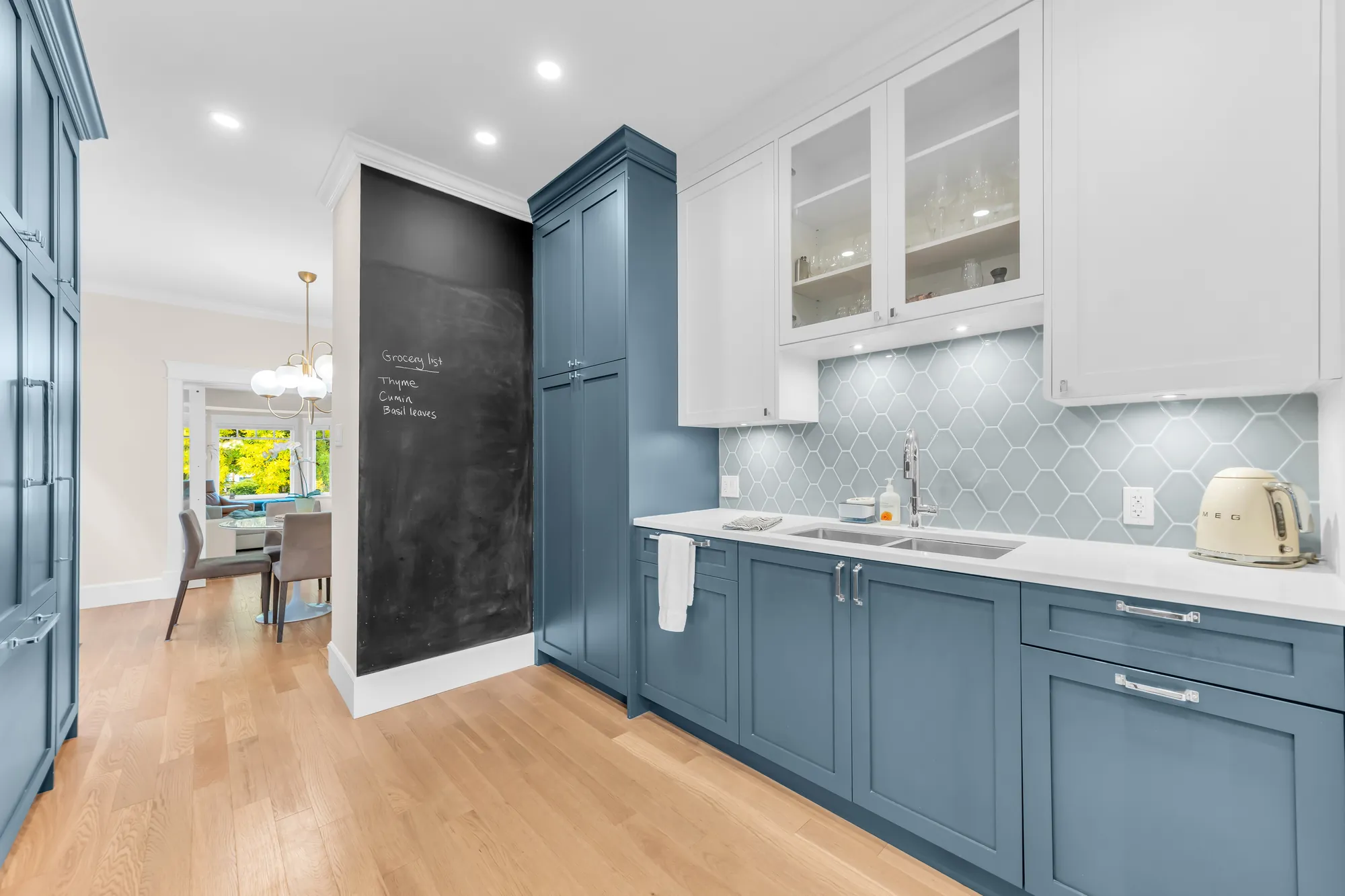 The sink wall with white upper cabinets, some glass-fronted, a wall painted as a chalkboard, the dining room beyond