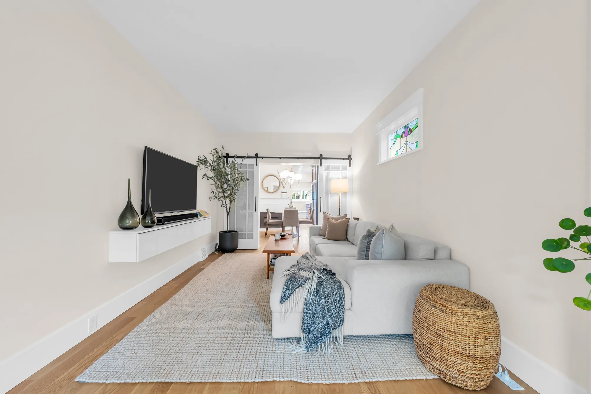 From the bay window toward the dining room: a television over a floating console, the sofa, sliding barn doors open to the dining room