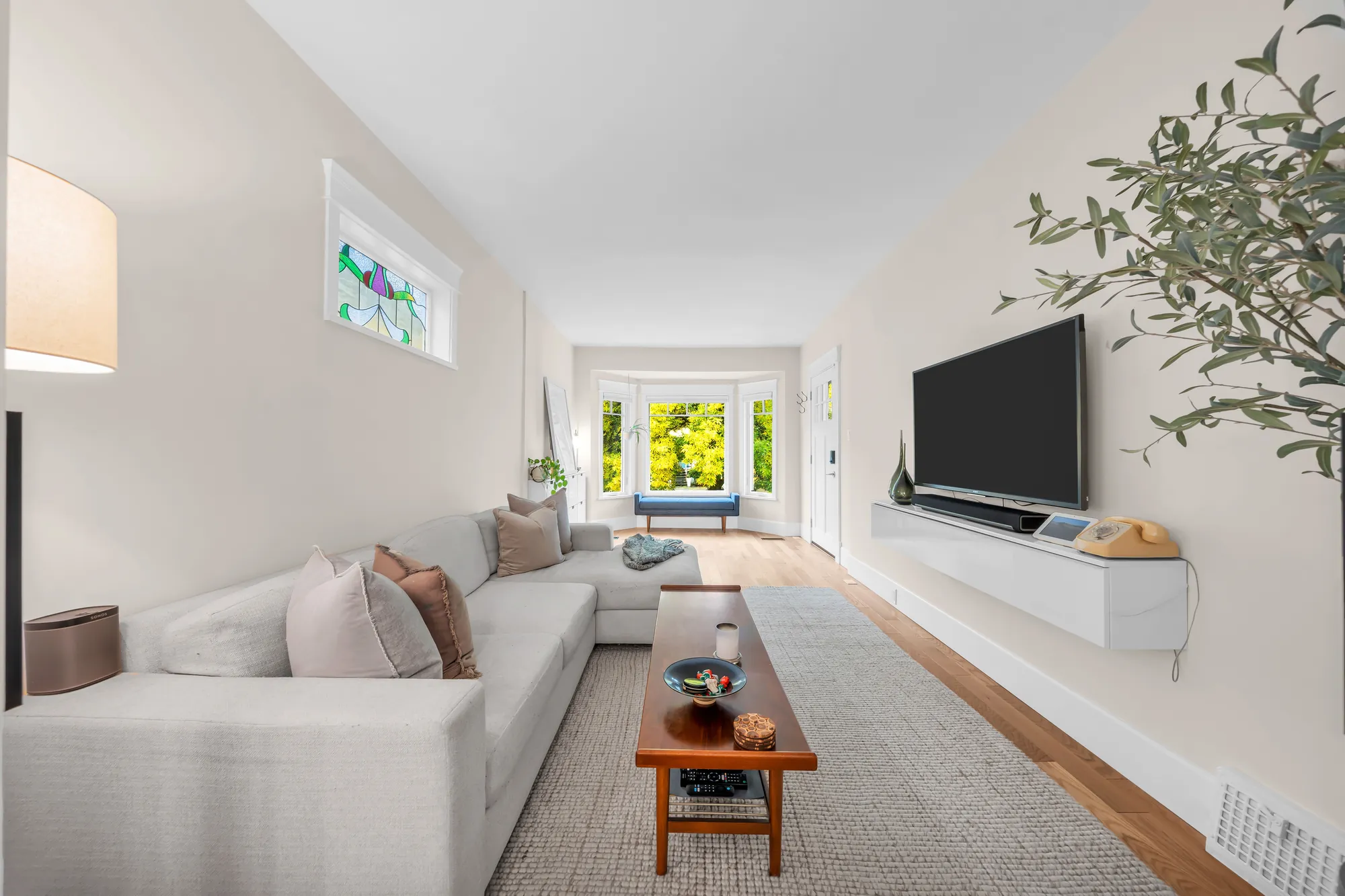 The living room from the dining room end toward the bay window: the sectional, the coffee table, the television on the wall