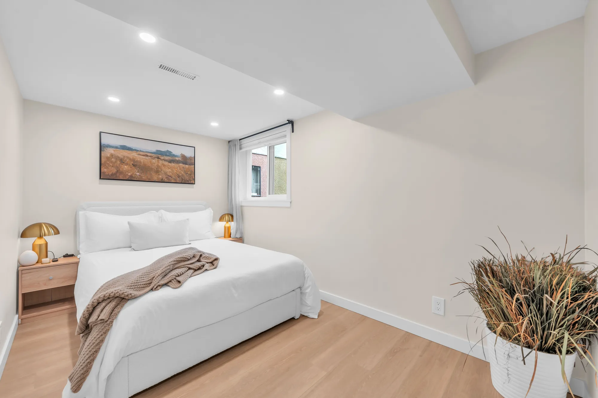 The lower bedroom: a bed with white linen, a framed landscape, a small window