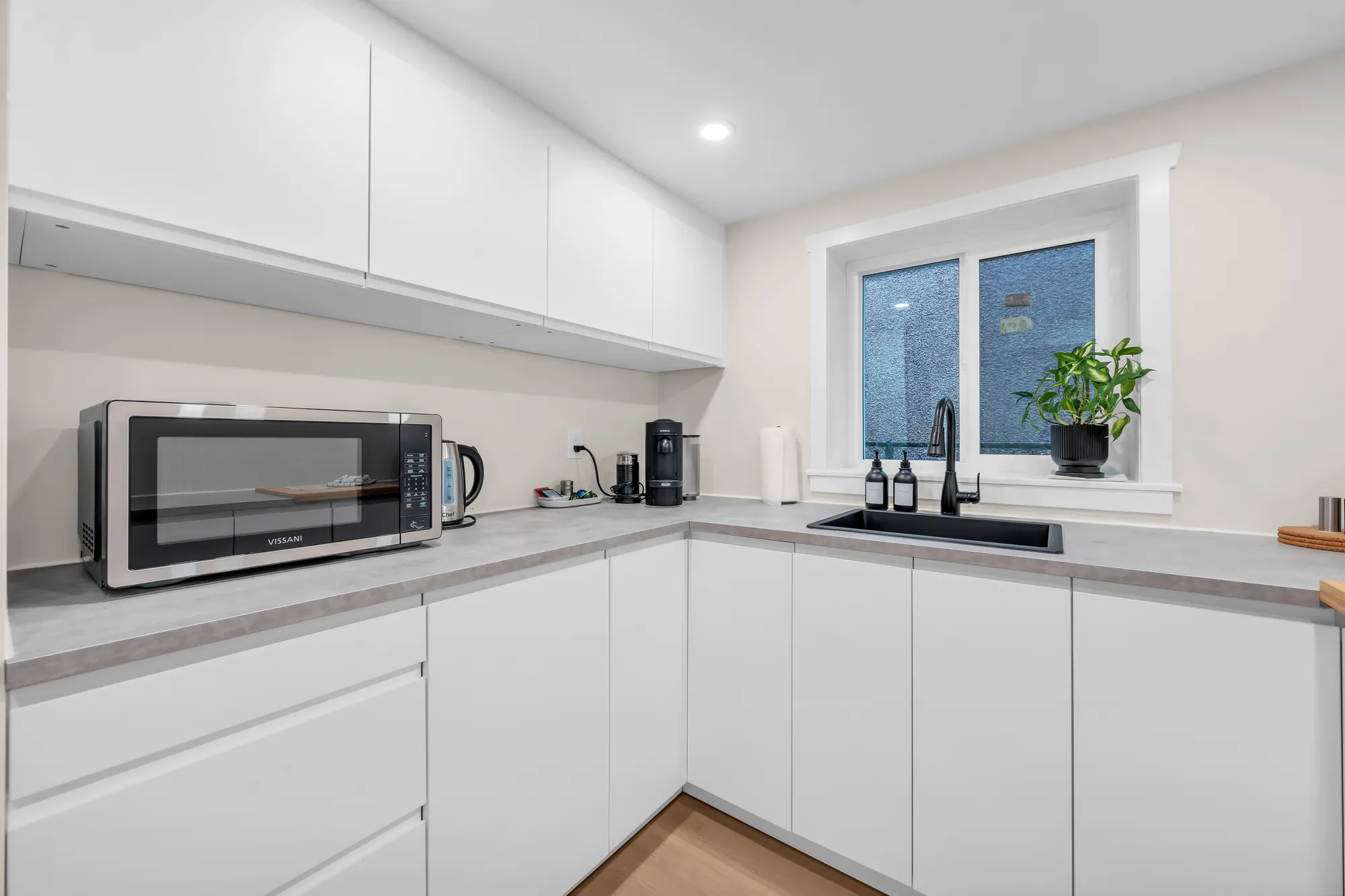 The lower kitchen counter with a microwave, the sink under the window