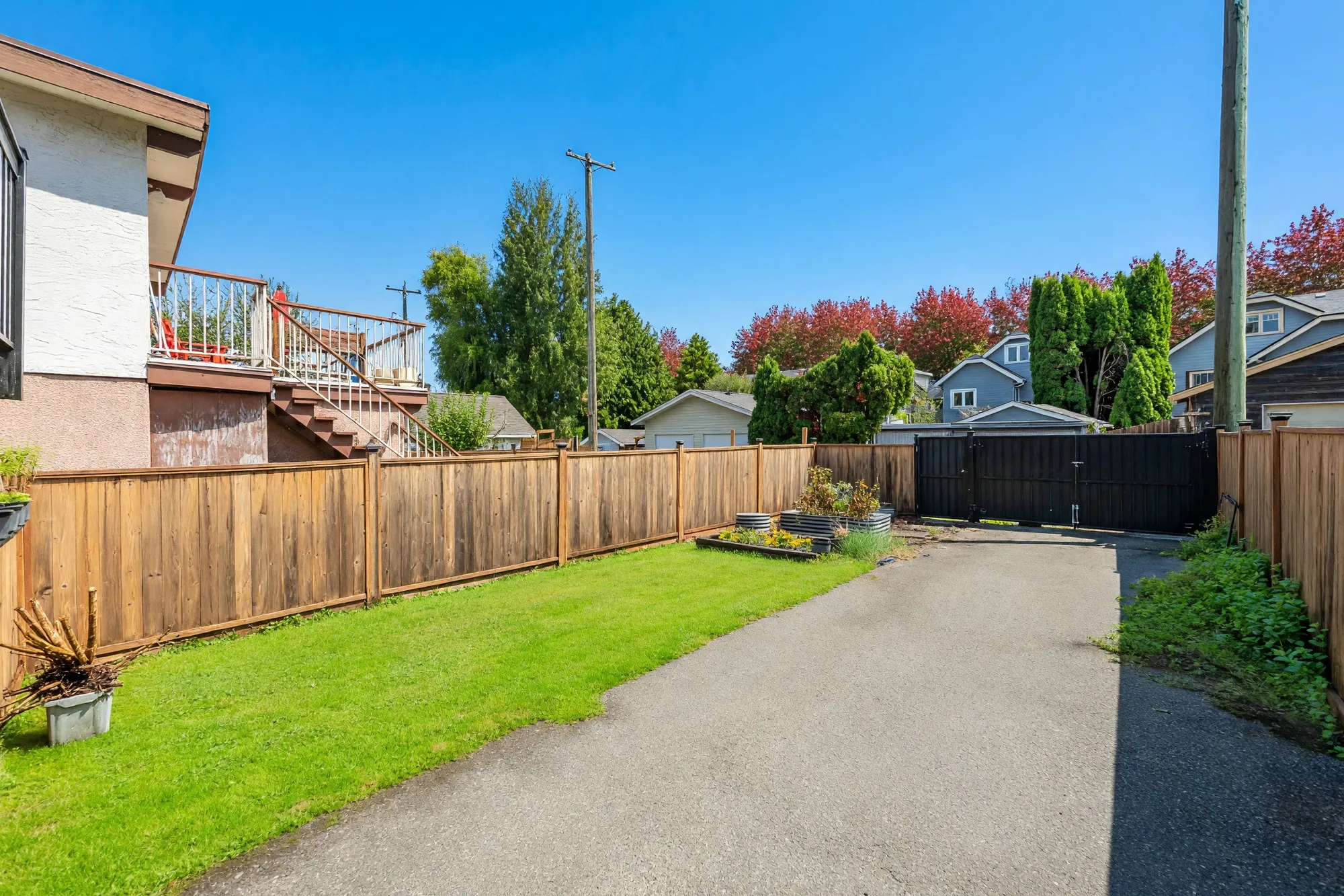 The paved parking pad beside the lawn, the board fence and the gate to the lane at the far end