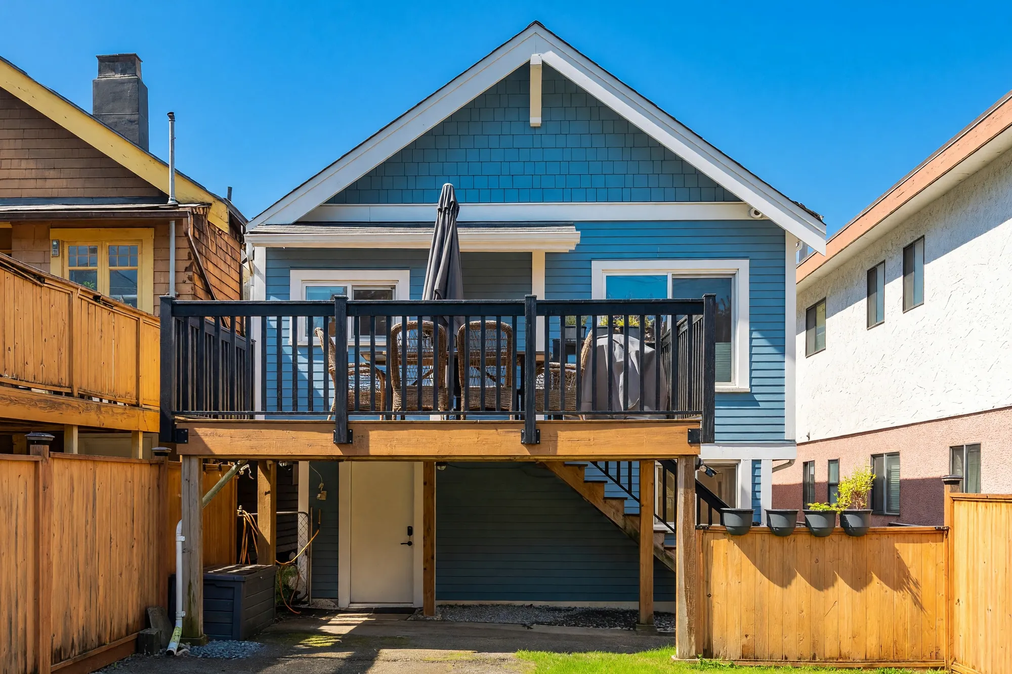 The back of the house: a deck with dark railings above the lower floor, a stair down to the yard, the door to the lower floor under the deck, wood fences on both sides