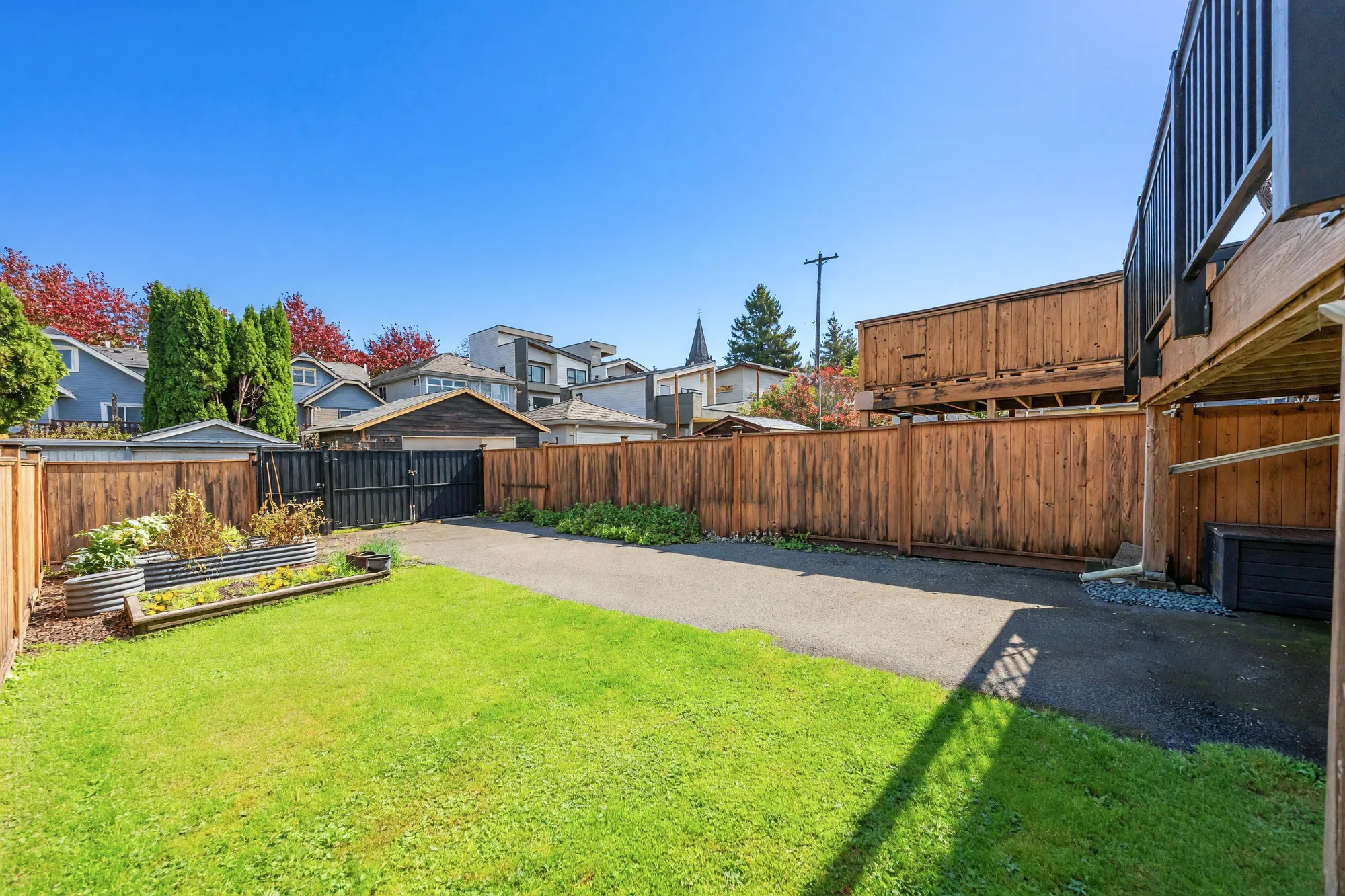 The lawn and the parking pad from beside the house, raised beds along the fence, the back gate